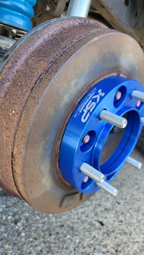 Close-up of a customer's blue 1-inch hubcentric wheel spacer installed on a vehicle's wheel hub.