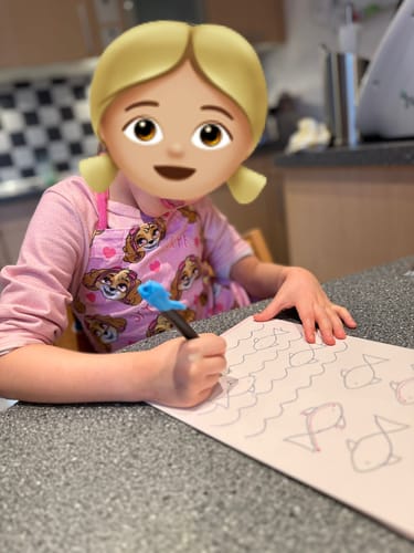 Eine Kundin zeigt ein Kind, das mit einem Stift in einem magischen Edubini Übungsheft Fische nachzeichnet.