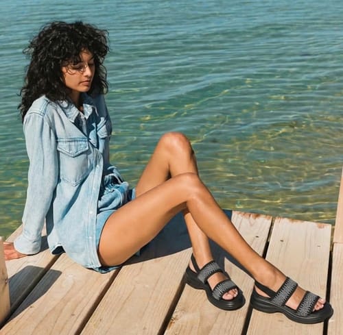 Reviewer sitting on a wooden dock wearing black platform Steady sandals with embellished straps.