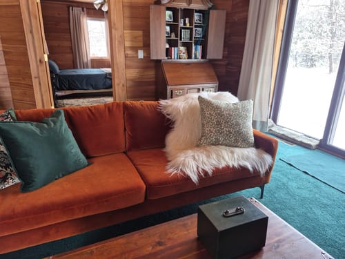 Reviewer's patterned pillow cover displayed on an orange couch in a cozy, wood-paneled room.