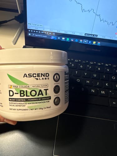 Reviewer holding a white tub of D-BLOAT in Pina Colada flavor in front of a laptop.