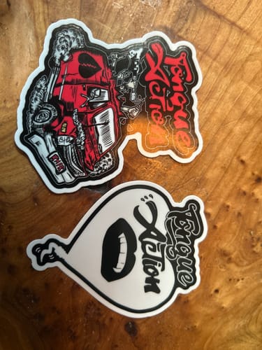 Customer's two custom vinyl stickers from the seasonal sale. One is red and black, the other is black and white, on a wood surface.