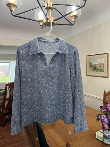Customer's finished long-sleeved blouse made from the dusty blue Floral Sachets rayon fabric, shown on a hanger.