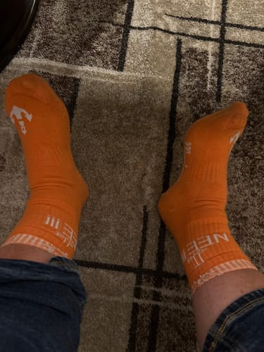 Ein Kunde trägt die leuchtend orangen Möwe Nee Socken mit weißem Schriftzug am Knöchel.