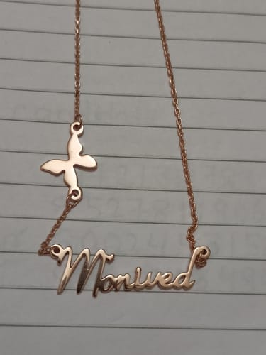 Customer's Rose Gold Personalised Butterfly Necklace with the name 'Monived' laid flat on a lined surface.