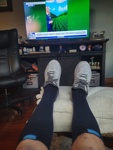 Customer's point of view, relaxing with their feet up while wearing black compression socks and sneakers.