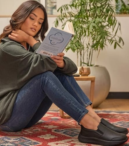 Reviewer sitting on a rug while wearing the black Dry Fit shoes and reading a book.