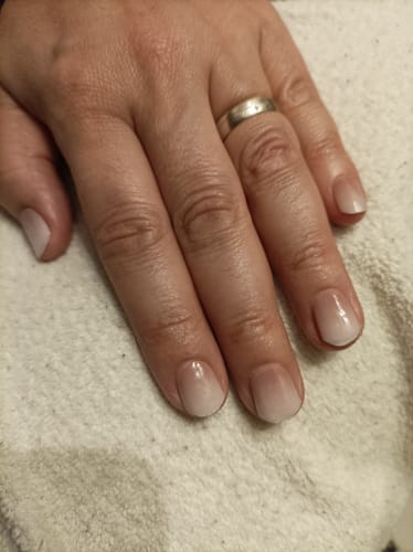Hand einer Kundin, die die 'Babyboomer Nude' UV Gel Wraps auf ihren kurzen Nägeln trägt.