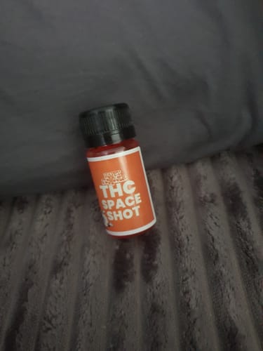 Rezensent zeigt das Fläschchen THC Space Shot Orange auf einer grauen, flauschigen Oberfläche.
