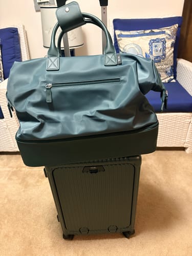Customer's teal weekender bag shown on top of a dark green rolling suitcase.