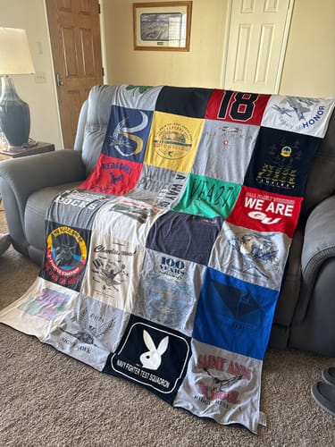 Customer's keepsake Project Repat T-Shirt Quilt made from various shirts, shown draped over a gray sofa.