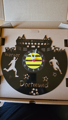 Kundenfoto der personalisierten Fussball Wanduhr 'Dortmund' aus schwarzem Vinyl, die im offenen Versandkarton liegt.