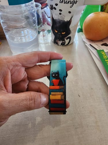 Customer's hand holding the Happy Here Watchband, showing its colorful cat and book design.