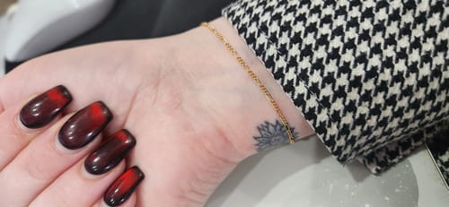 Close-up of a customer's wrist wearing a delicate gold Sparked permanent bracelet from FinerRings.
