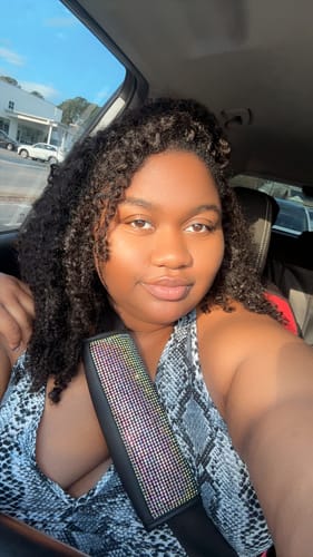 Reviewer in a sunlit car wearing the soft, curly Ywigs Burmese Water Crochet Hair.