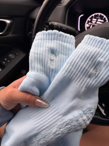 A customer holds up a pair of baby blue ribbed Dual-Direction Grip Basics socks, showing the grips on the bottom.