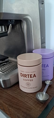 Customer's tan DIRTEA Coffee canister on a wooden counter next to a coffee machine and a measuring spoon.