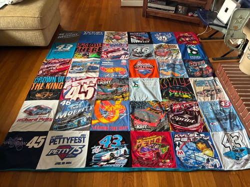 Customer's Project Repat T-Shirt Quilt made from colorful racing t-shirts, spread out on a wood floor.