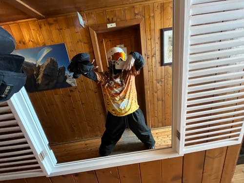 Customer takes a mirror selfie wearing their baggy black Snow Pants as part of a snowboarding outfit.