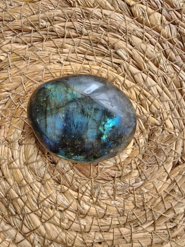 Customer's polished, iridescent monthly crystal resting on a woven surface.