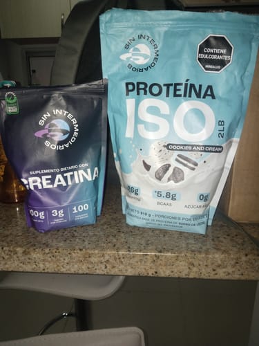El cliente muestra la bolsa de Creatina Monohidrato junto a la Proteína ISO, ambos productos sobre una encimera.