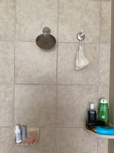Customer's Soap Pouch hanging from a hook in a tiled shower among other products.