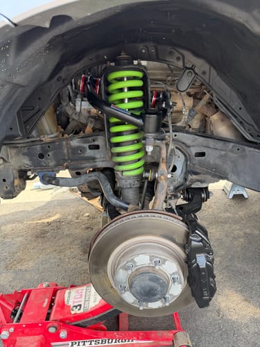 Customer's black upper control arms installed in a truck's wheel well with a bright green coilover.