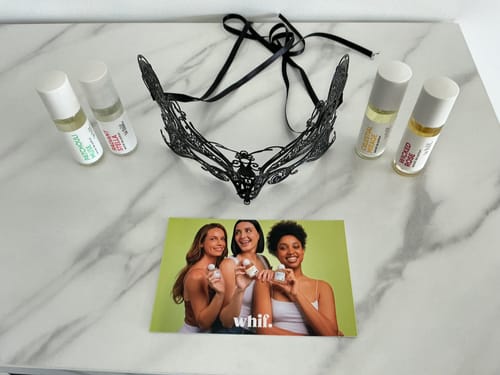 Customer's Patchouli Muse roll-on fragrance displayed with other scents and a black lace mask on a marble surface.