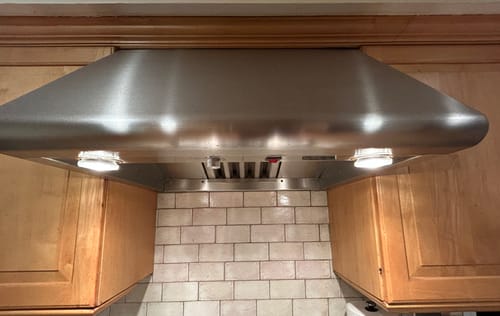Reviewer's PAR20 halogen bulbs installed in a range hood, emitting a warm light and protruding slightly.