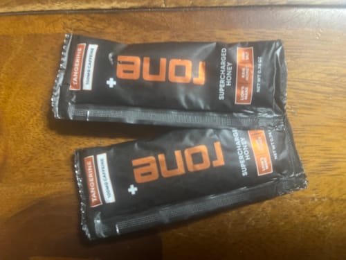 Customer's close-up view of two Tangerine SuperCharged Honey packets on a wood table.