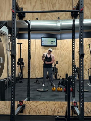 Reviewer flexing their muscular bicep in a gym mirror, showing their physique after using UGLYFACE® PUMP.