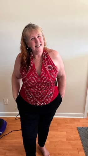 Reviewer smiling while wearing the red bandana-print halter top with black pants indoors.