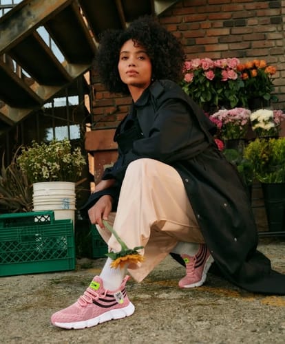Reviewer showcasing their pink Easy Step sneakers while crouching outdoors in a stylish outfit.