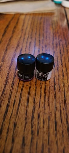 Customer's two small black jars of Chapter 2: Black Heart product sitting side-by-side on a dark wooden surface.