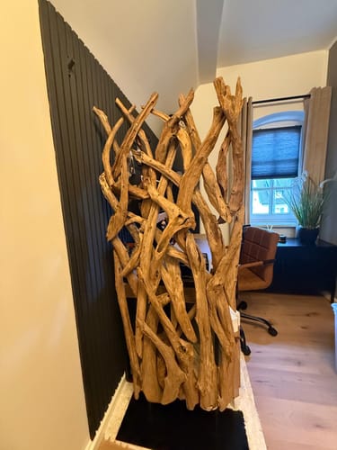 Kunde zeigt den schönen Raumteiler aus Teakholz in einem Zimmer neben einer dunklen Wand.