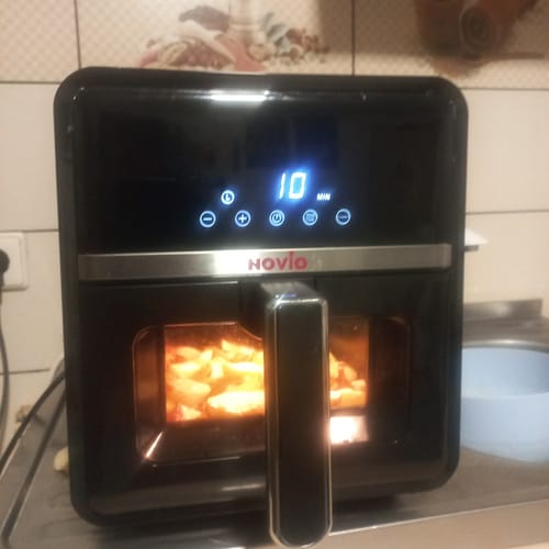 Un client arată air fryer-ul negru Novio StonePro în timp ce gătește cartofi în coșul iluminat.