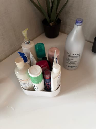 Anmelders hvite, kvadratiske snurrebrett fylt med toalettsaker på kanten av et badekar.