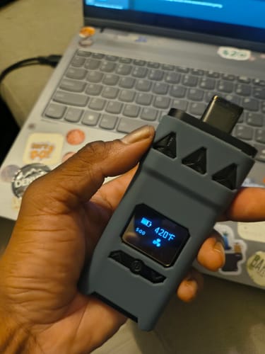 Customer holding the AirVape X with a grey X Shell on it. The lit screen shows the temperature is 420°F.