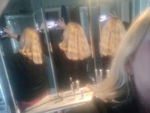 Kundin zeigt ihr schulterlanges, welliges Haar in einer Spiegelreflexion nach der Anwendung der Apple-Wonder Haarseife.