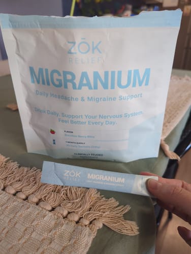 Reviewer holds a single-serving Migranium stick pack in front of the larger supply pouch on a table.
