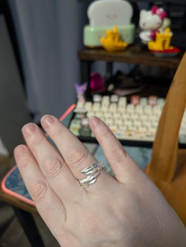 A reviewer's hand wearing the silver Feather From An Angel Ring, which wraps around the finger.