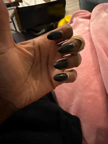 A reviewer's hand showing the dark, almond-shaped Stiletto press-on nails.