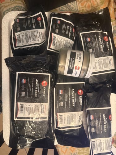 Reviewer's LOCASH Premium Angus Steak Bundle unboxed in its cooler, showing various steaks and a seasoning jar.