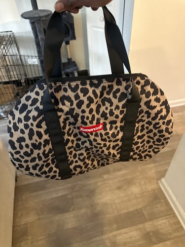 A reviewer holding the cheetah-print CHEETAH Duffle Bag by its black straps.