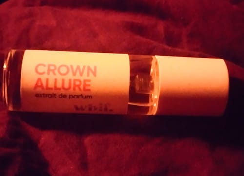 Close-up of a customer's Crown Allure perfume bottle lying sideways on a dark red fabric.