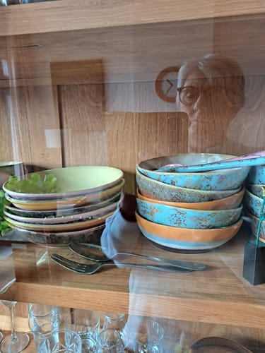 Recensent toont een verzameling kleurrijke HKliving 70's borden, gestapeld in een houten vitrinekast.