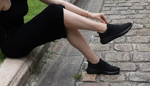 Customer adjusting their black Air Glide shoe while sitting on a cobblestone path.