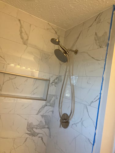 Reviewer's newly installed 1-Spray Dual Shower Head Set in a modern, marble-tiled shower stall.