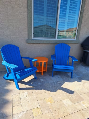 Customer's two bright blue folding Adirondack chairs set up on a stone patio with an orange side table between them.