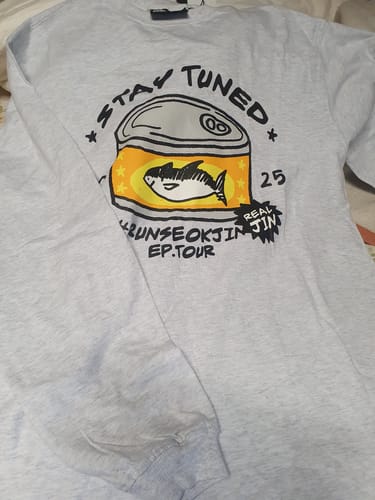 Customer's grey long-sleeved BTS Jin t-shirt laid flat, showing the cartoon tuna can graphic on the front.